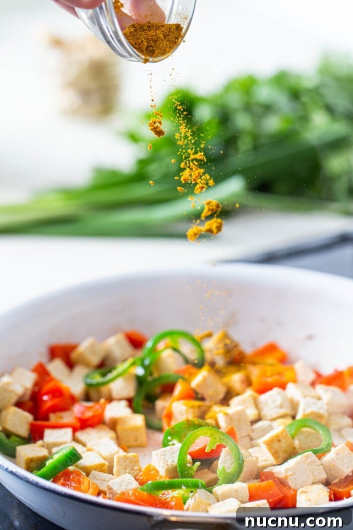 Essential Vegan Pantry Staples for Everyday Cooking 10 Curry powder being sprinkled into a skillet of tofu and veggies.