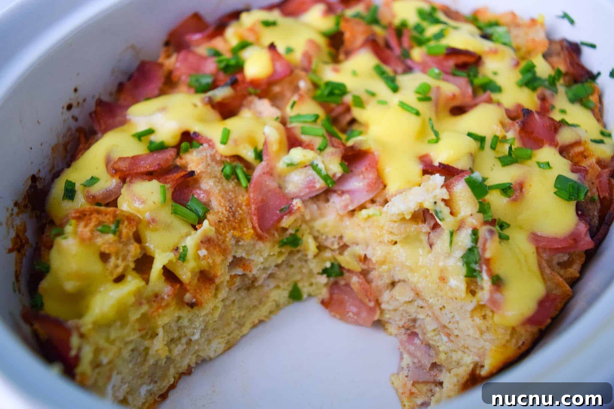 Overnight Eggs Benedict Casserole Recipe for Brunch Crowd 3 Overnight Eggs Benedict Casserole in white dish with piece missing close up