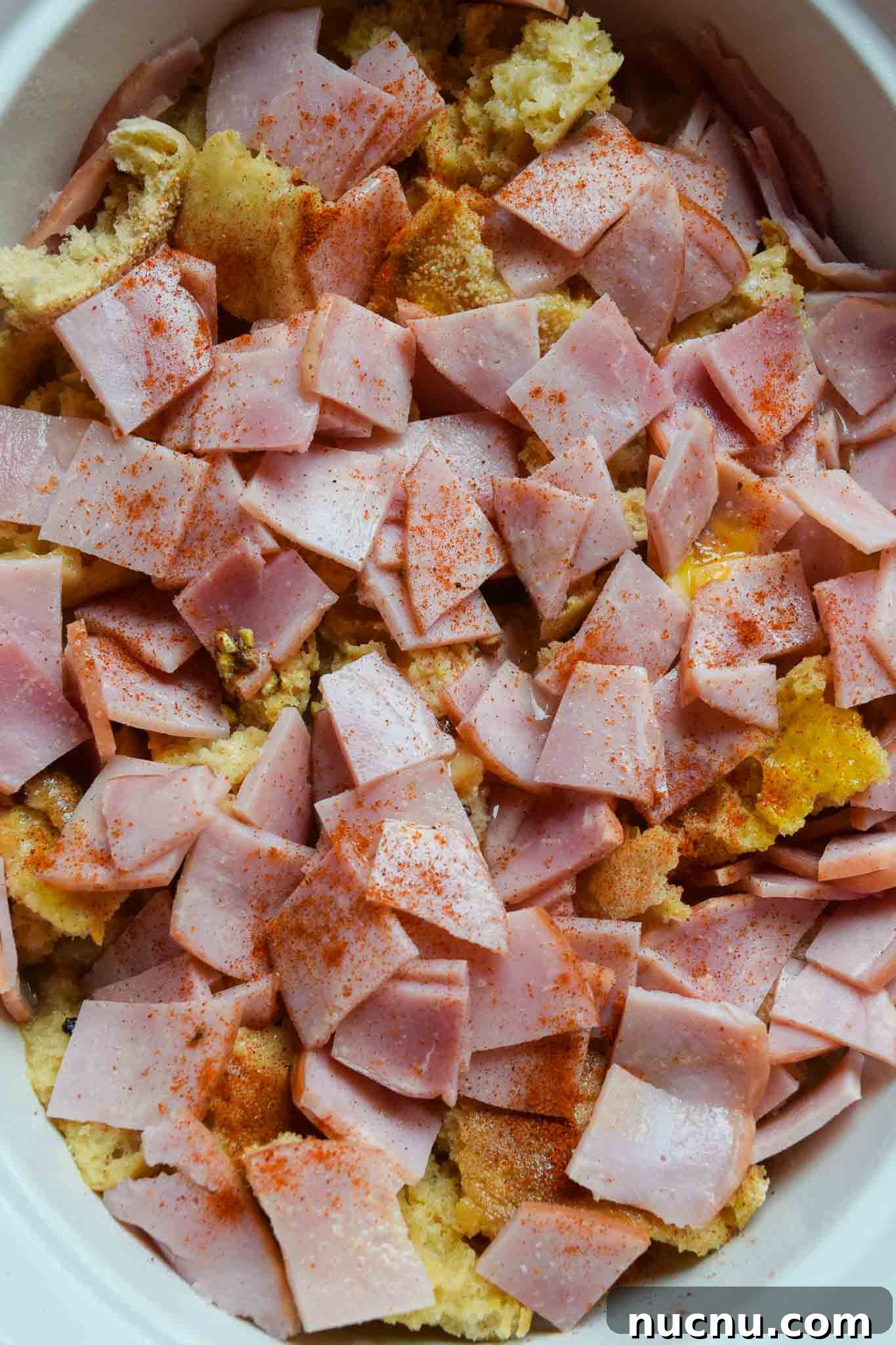 Overnight Eggs Benedict Casserole Recipe for Brunch Crowd 4 Overnight Eggs Benedict Casserole topped with bacon in white dish overhead shot
