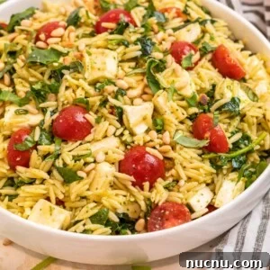 Pesto orzo salad in white bowl topped with freshly chopped basil and toasted pine nuts.