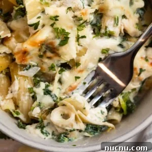 Chicken spinach and artichoke pasta casserole in dish with fork.