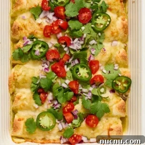 Pan of green chicken enchiladas topped with onion, cilantro, tomatoes, etc.
