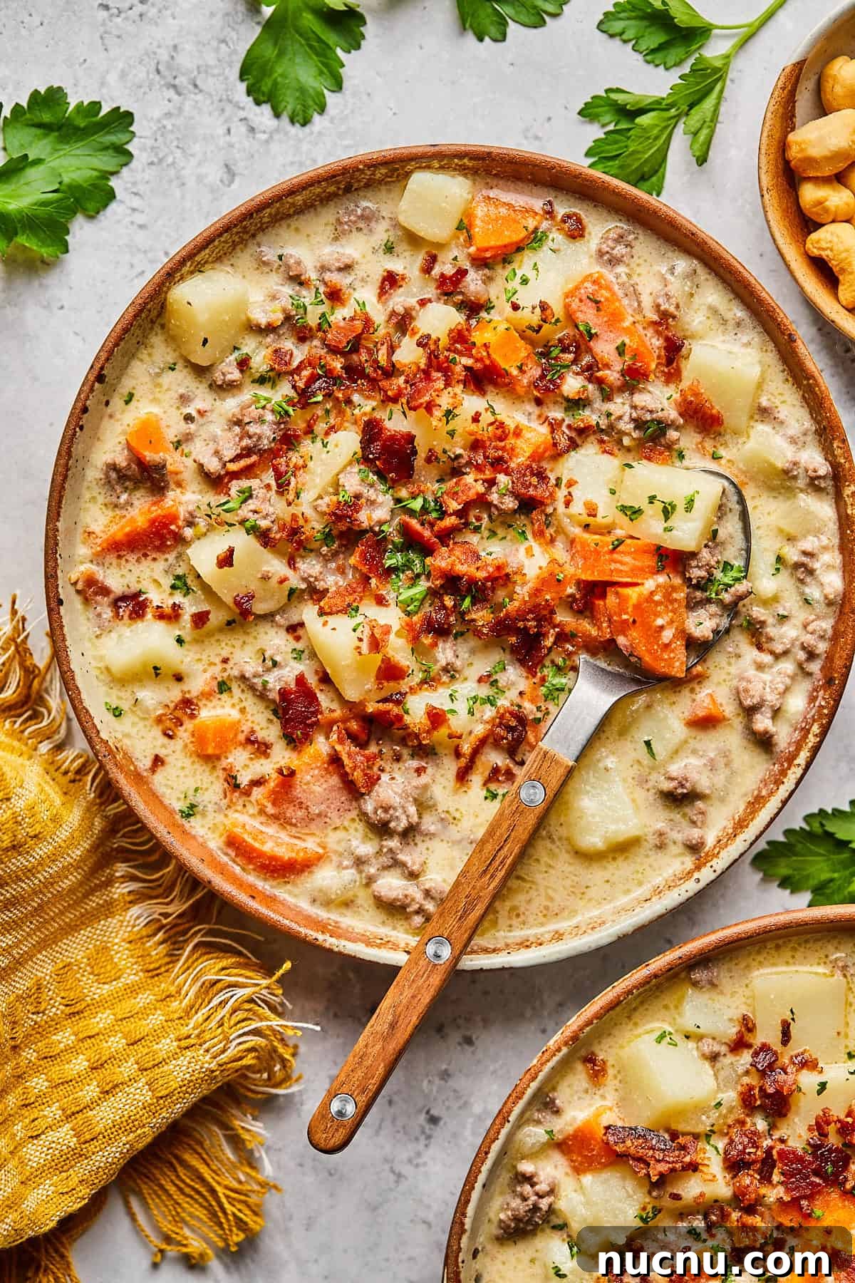 dairy free cheeseburger soup topped with bacon in a bowl with a wooden and metal spoon