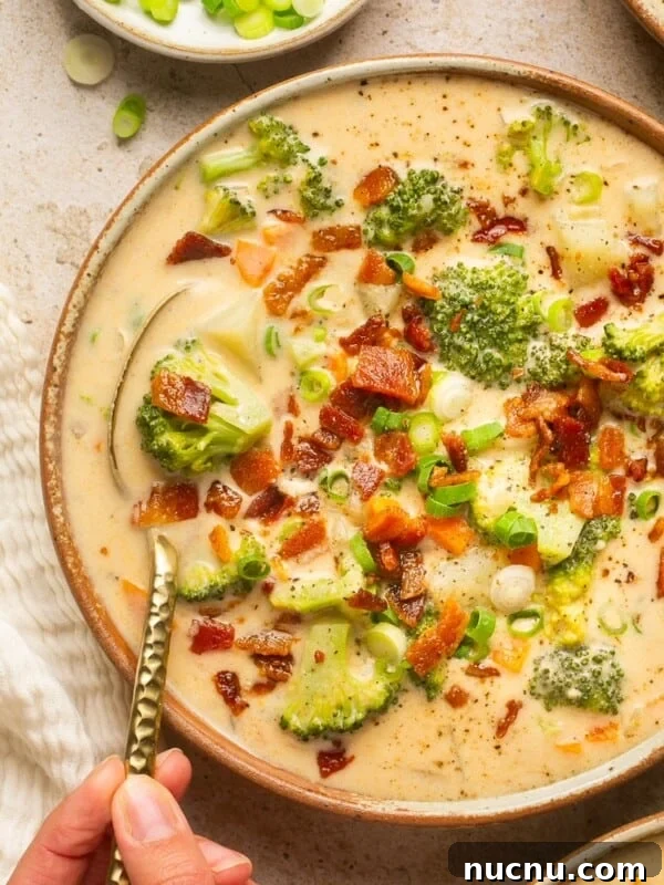 loaded broccoli cheese & potato soup in a bowl with a spoon taking a bite out