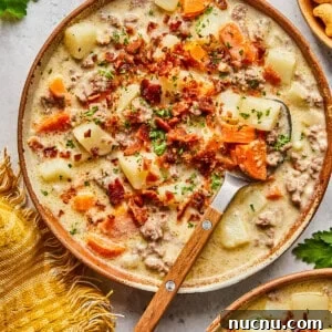 dairy free cheeseburger soup topped with bacon in a bowl with a wooden and metal spoon