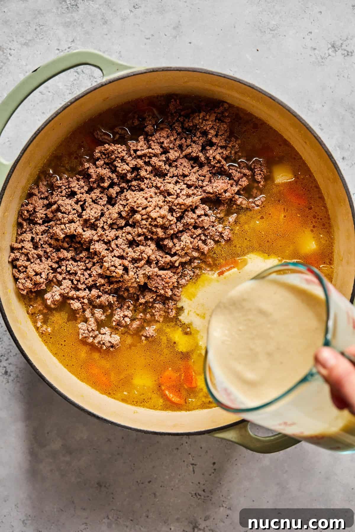 cashew cream being poured into a pot with ground beef and broth