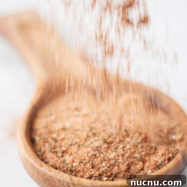 Savory Pork Butt Dry Rub Recipe for Juicy Barbecue 10 cajun spice sprinkling over large wooden spoon filled with brownish red cajun spice seasoning