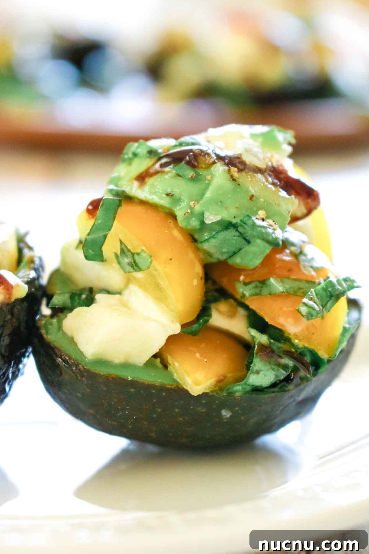 Avocado stuffed with caprese salad of mozzarella and tomatoes and drizzled with balsamic glaze on a white plate.