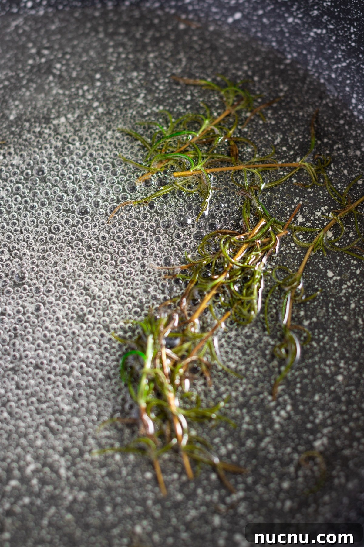 Fresh rosemary simmering in a grey pan on the stovetop.