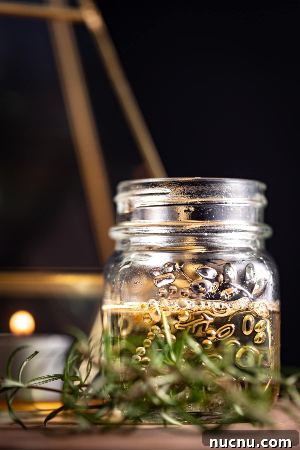 Syrup in a small glass jar, with fresh rosemary herbs in front of it, on a black background.