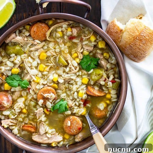 Cajun Chicken and Barley Gumbo Recipe for Comforting Flavor 3 Gumbo soup in a copper bowl with a spoon and bread pieces.