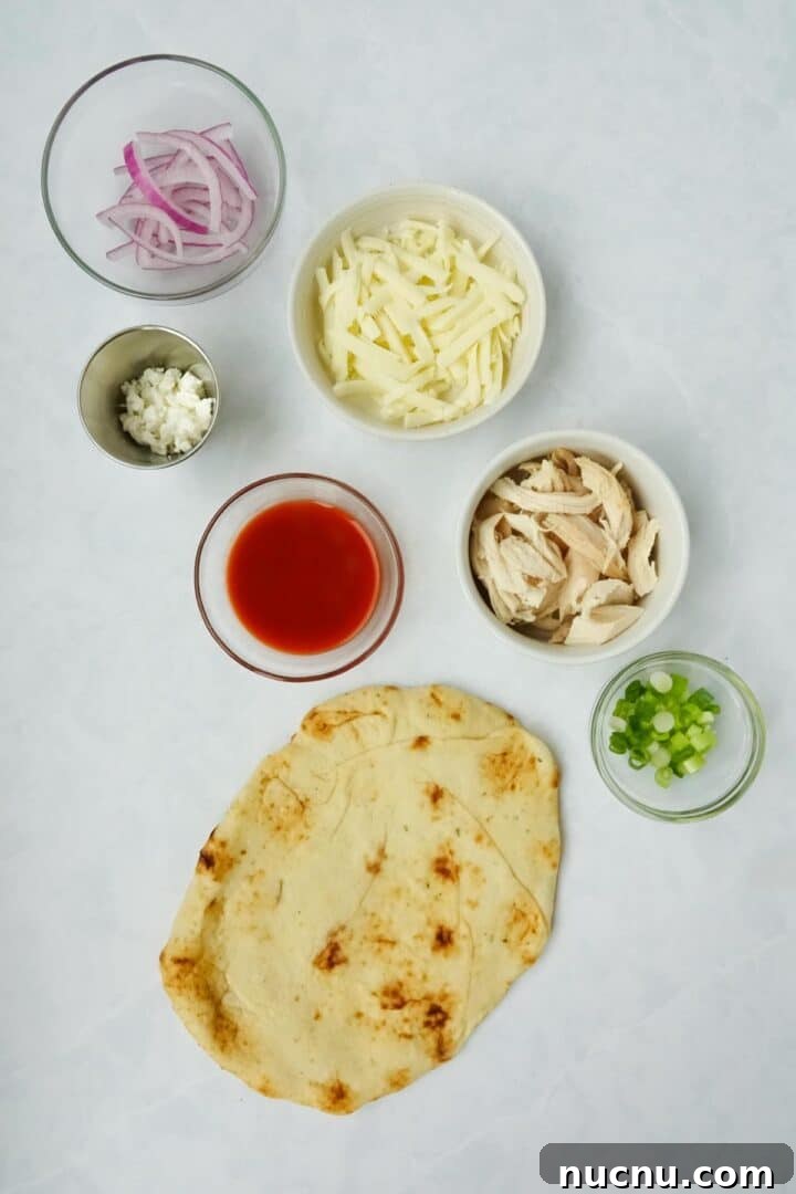 Spicy Buffalo Chicken Flatbread Pizza Recipe for Game Day 3 Ingredients for buffalo chicken flatbread displayed on a white marble counter including flatbread, cooked chicken, green onions, red onions, mozzarella cheese, buffalo sauce, and feta cheese