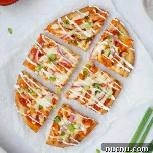 Spicy Buffalo Chicken Flatbread Pizza Recipe for Game Day 5 Whole buffalo chicken flatbread topped with green onions, red onions, and a drizzle of sour cream displayed on parchment paper on a white counter