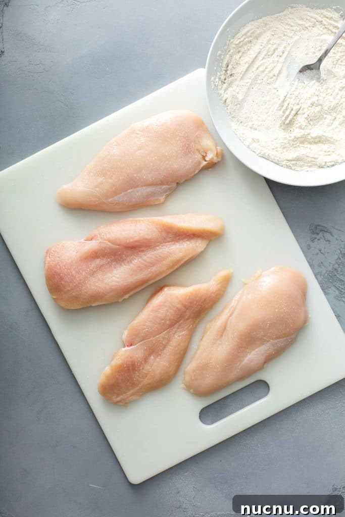 two chicken breasts cut in half lengthwise over a white cutting board