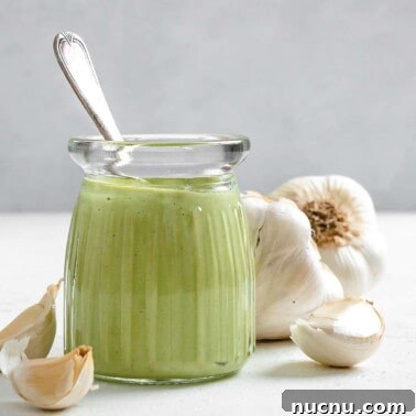 completed Creamy Vegan Garlic Sauce in a glass jar with garlic in the background