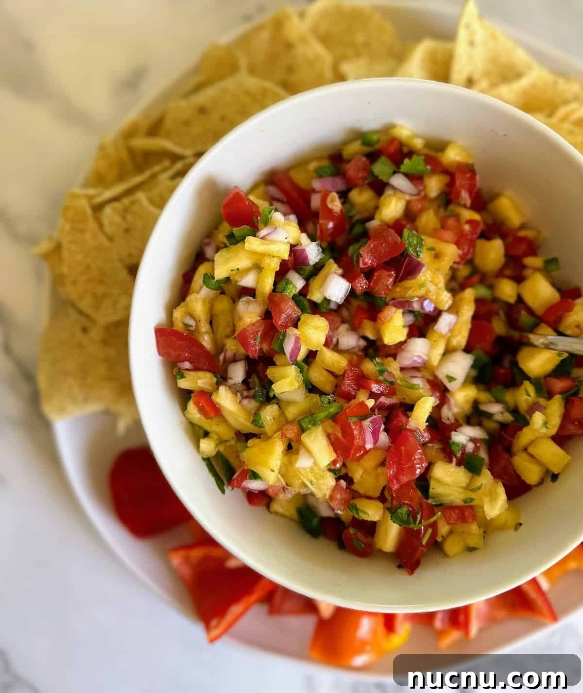 Easy pineapple salsa ina bowl served with tortilla chips and baby bell peppers. 