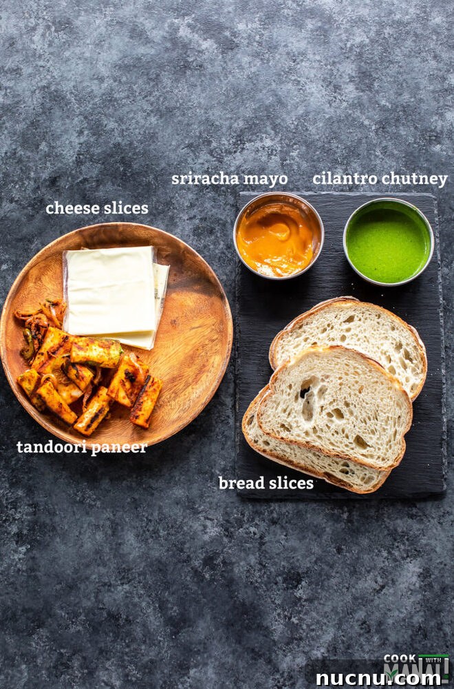 2 bread slices, a bowl of chutney, 2 cheese slices, paneer pieces all placed on a board