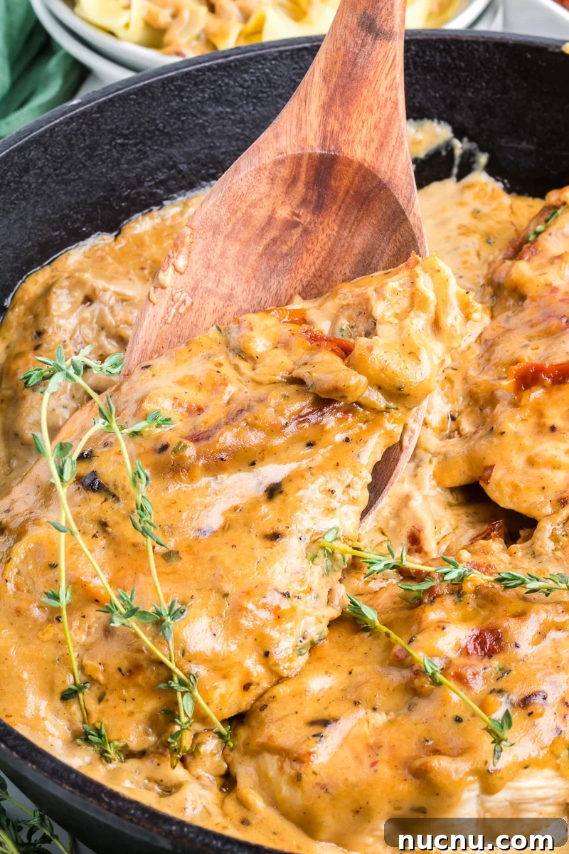 A spoon is scooping up a piece of marry me chicken from a cast iron skillet.
