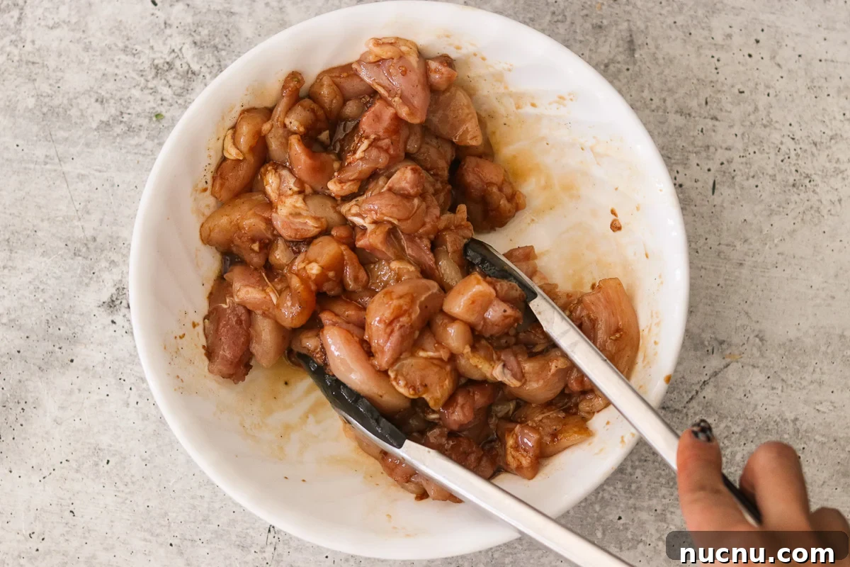 Hibachi Chicken Bowl Recipe — Japanese Steakhouse Copycat 4 Tongs tossing cubed chicken in tamari, sesame oil, garlic, ginger, and black pepper.