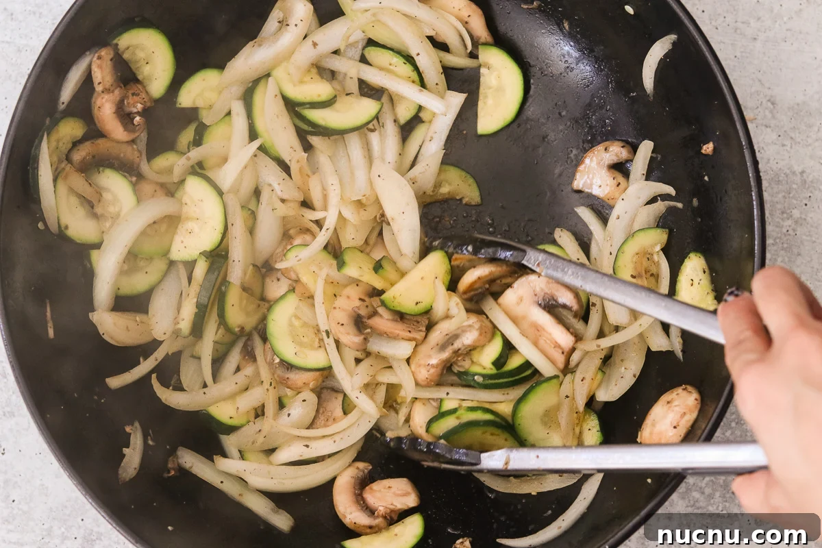 Hibachi Chicken Bowl Recipe — Japanese Steakhouse Copycat 5 Sliced onion, zucchini, and mushrooms cooking in avocado oil in a large skillet; tongs are being used to toss them.