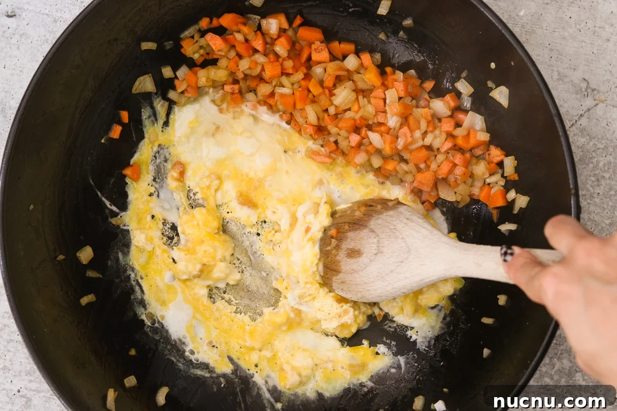 Hibachi Chicken Bowl Recipe — Japanese Steakhouse Copycat 7 Eggs cracked into the skillet beside the vegetables being scrambled with a wooden spoon.