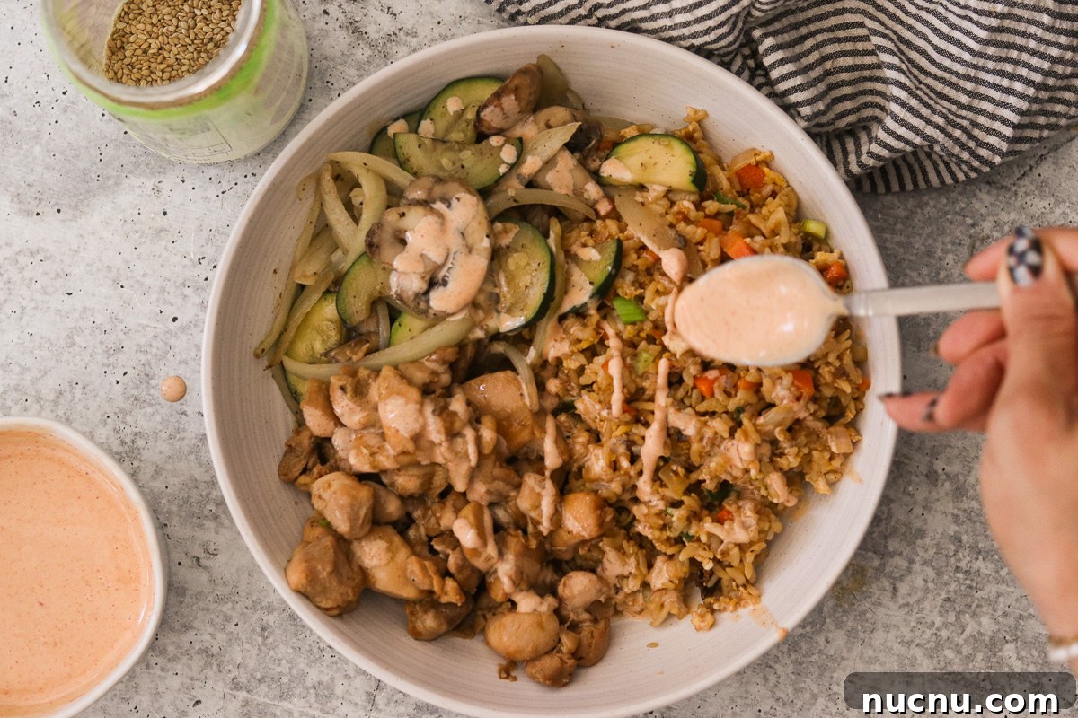 Hibachi Chicken Bowl Recipe — Japanese Steakhouse Copycat 10 Hibachi chicken in a bowl with fried rice and vegetables, being topped with yum yum sauce.