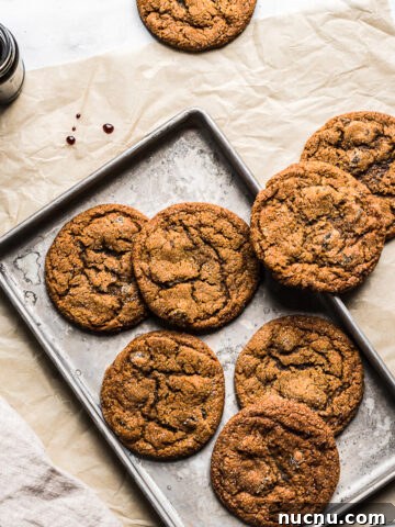 Ginger cookies on a baking sheet resting on a brown parchment paper rectangle. A jar of molasses is nearby.