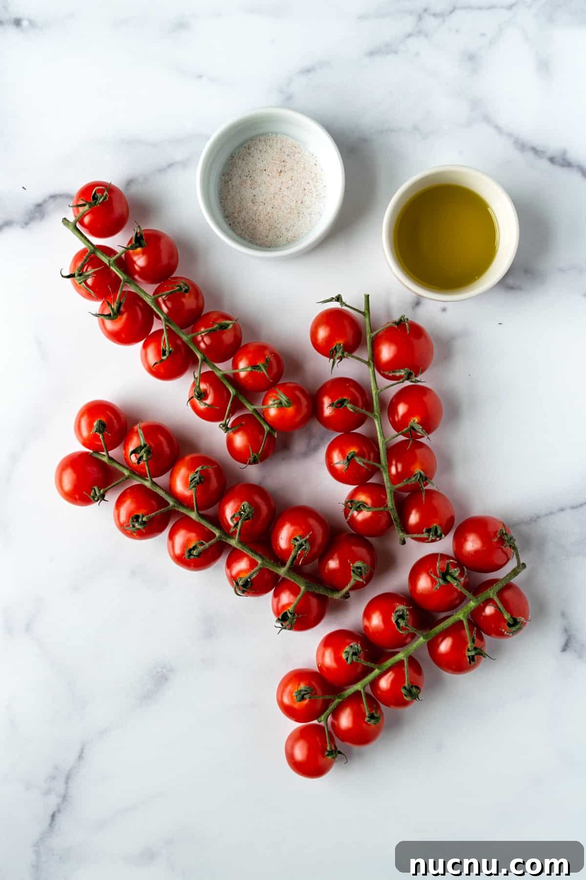 Tomatoes on the vine, olive oil, and sea salt on a marble countertop.