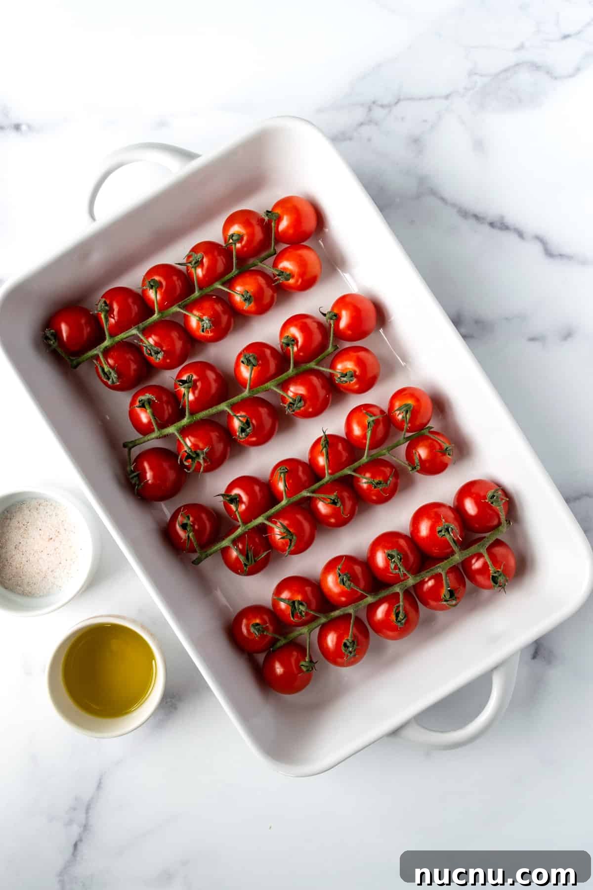 Cherry tomatoes on the vine in a white baking dish with olive oil and sea salt.