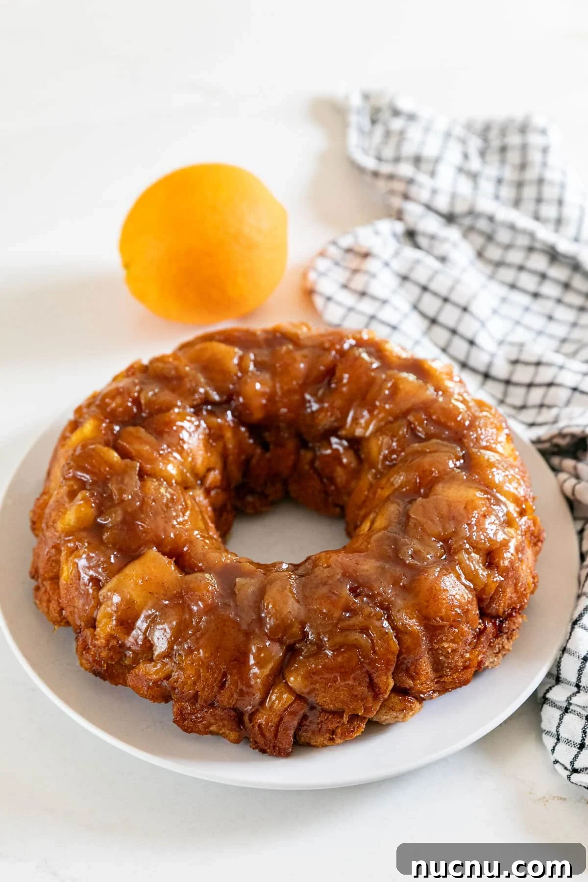 Orange Cinnamon Pull-Apart Loaf: Zesty Sweet Morning Bread 2 A bundt shaped orange monkey bread on a white plate with an orange and black and white checked napkin behind it.