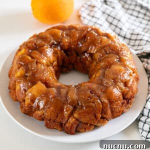 A bundt shaped orange monkey bread on a white plate with an orange and black and white checked napkin behind it.