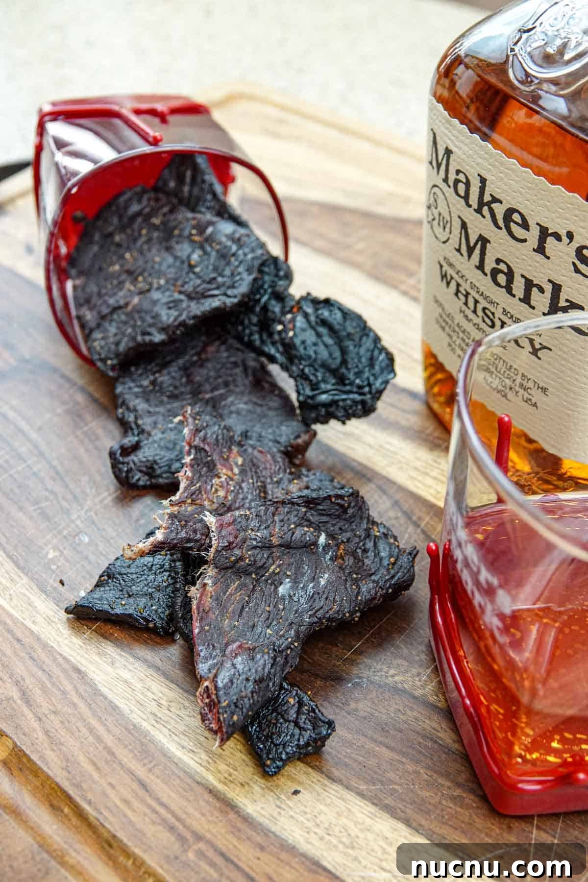 Kentucky Bourbon–Glazed Beef Jerky Recipe 2 Beef jerky in bourbon glass with bottle of makers mark bourbon