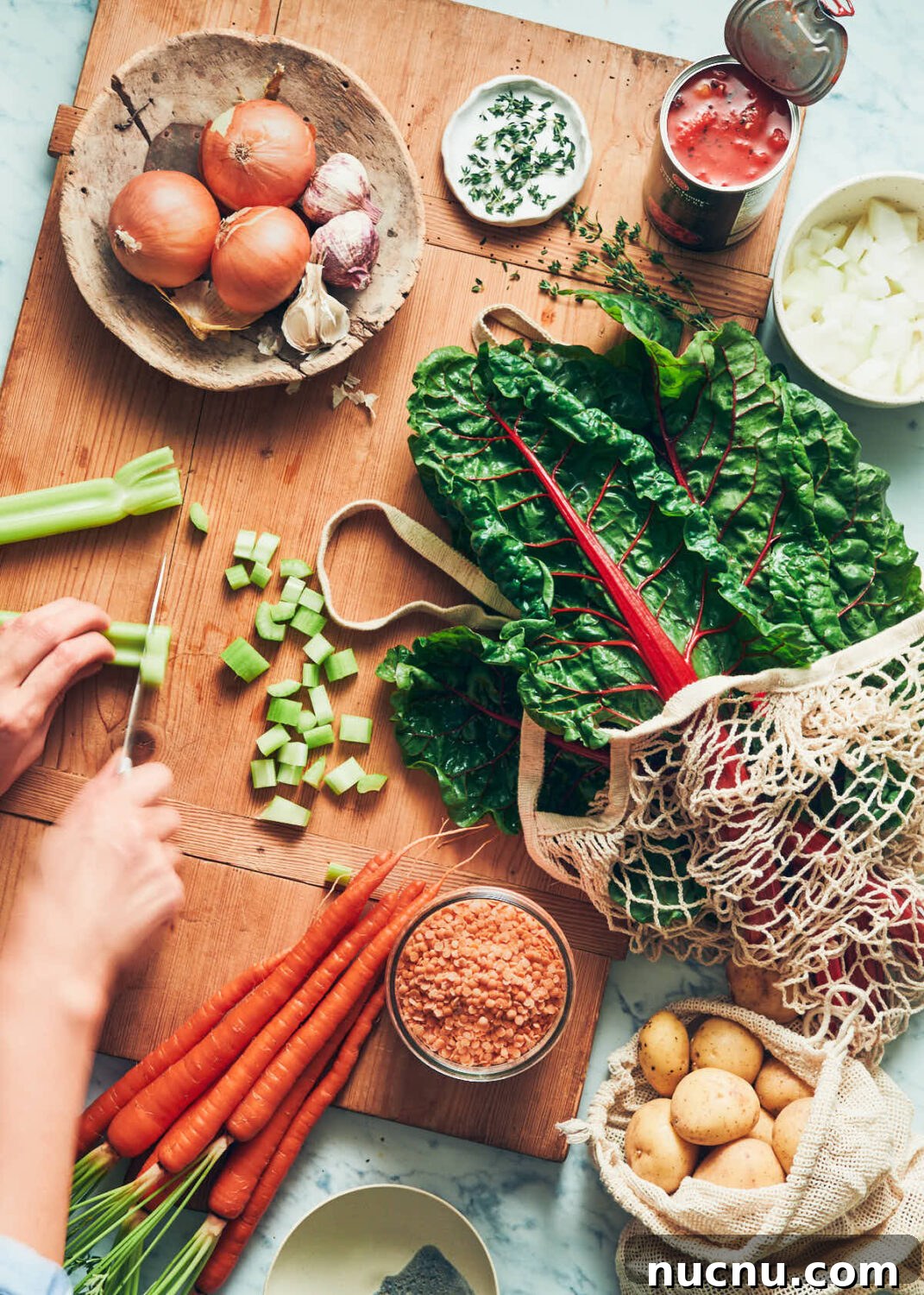 Ingredients for vegan red lentil soup like onions, garlic, celery, carrots, swiss chard, red lentils and potatoes on a cutting board