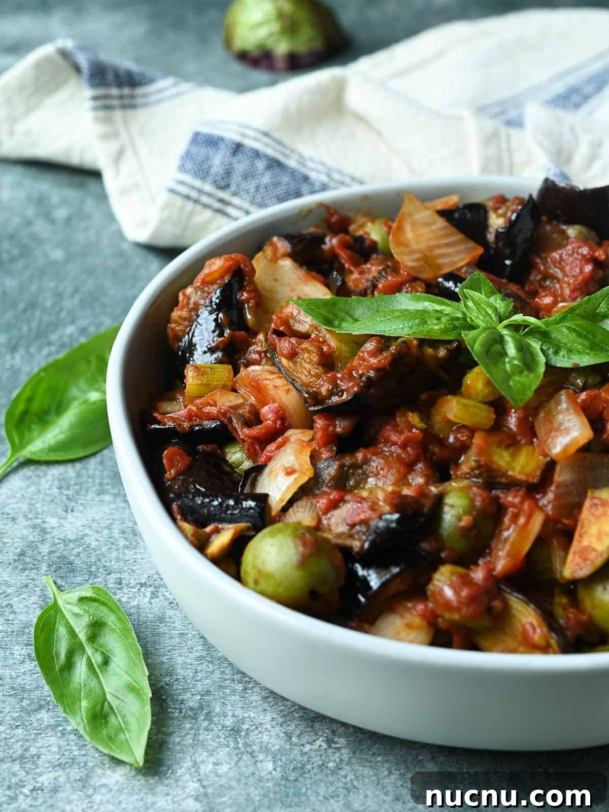 Sicilian Eggplant Caponata Recipe: Sweet-Sour Mediterranean Relish 2 Eggplant caponata in a white bowl with basil leaves to the left.