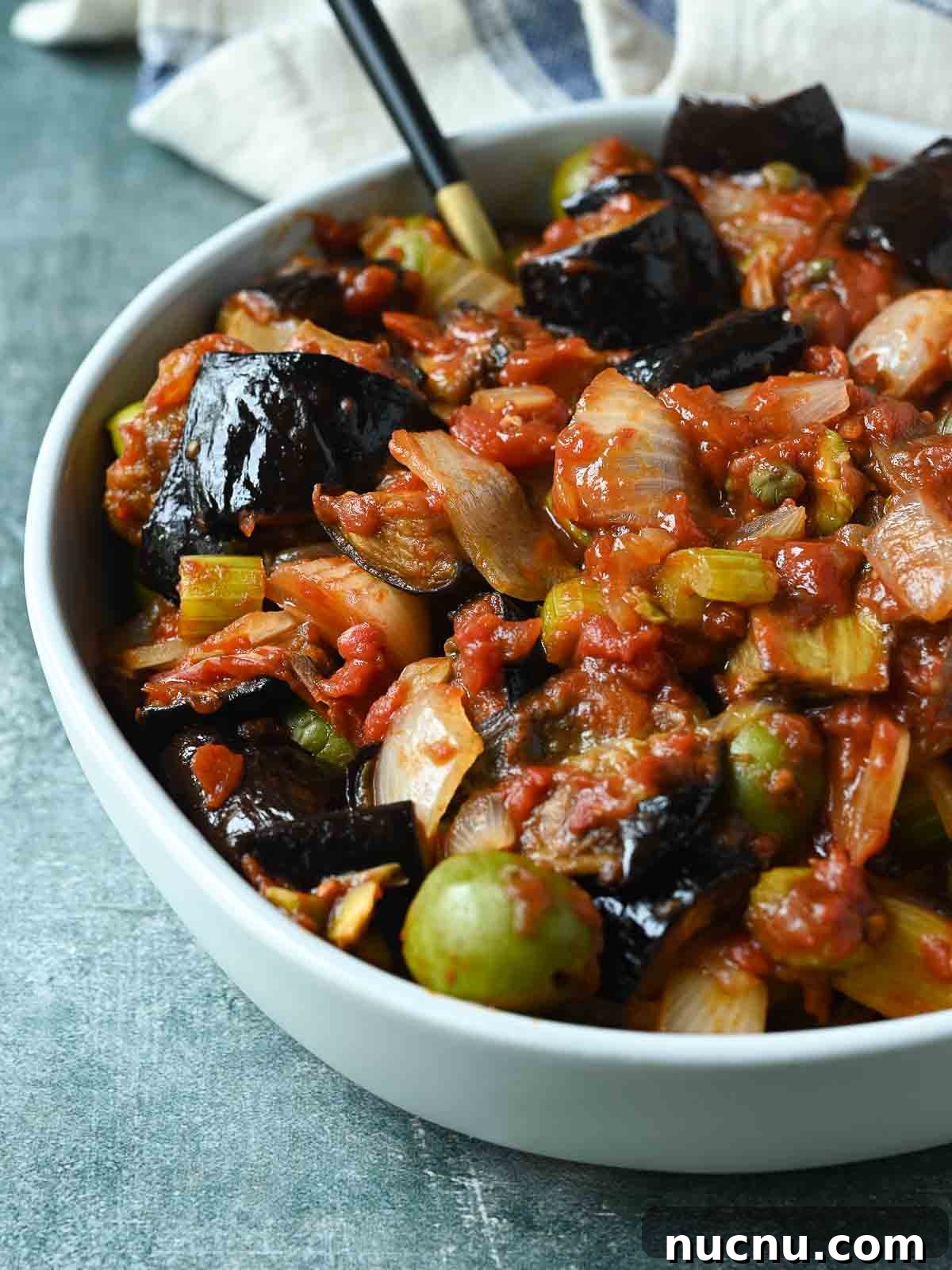 Sicilian Eggplant Caponata Recipe: Sweet-Sour Mediterranean Relish 8 Eggplant caponata in a white bowl on a blue surface.