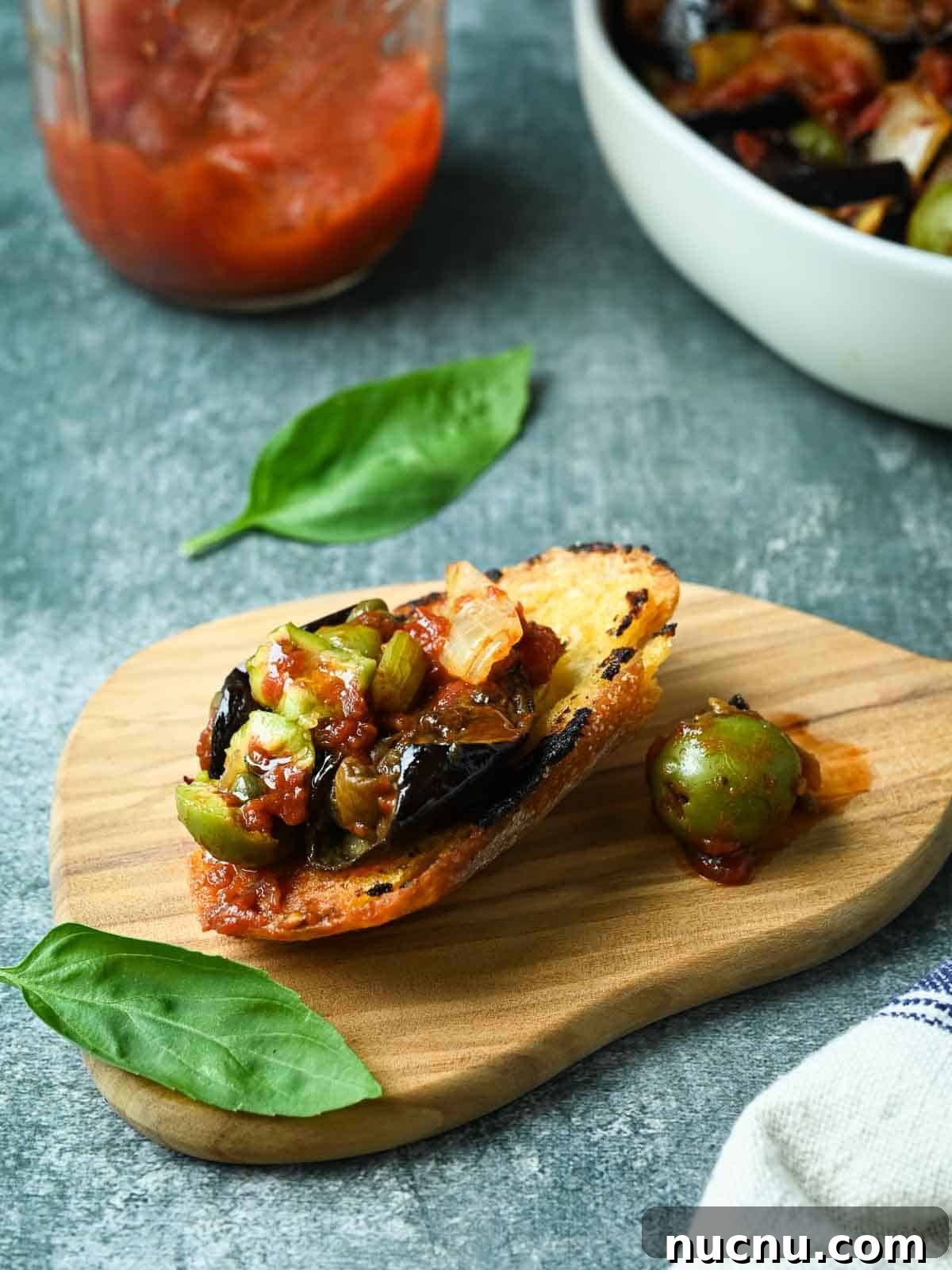 Sicilian Eggplant Caponata Recipe: Sweet-Sour Mediterranean Relish 9 Piece of bread with caponata spread on it with basil and sauce on the side.