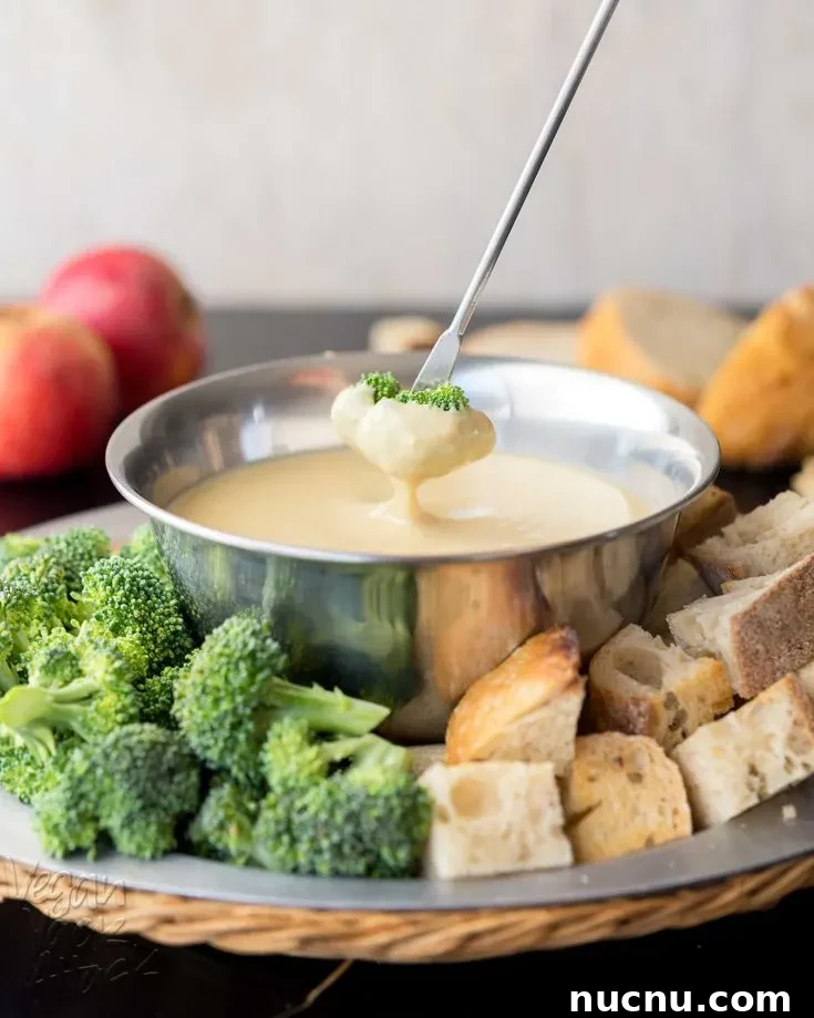 pale fondue dip in a metal bowl with chopped broccoli and bread around it