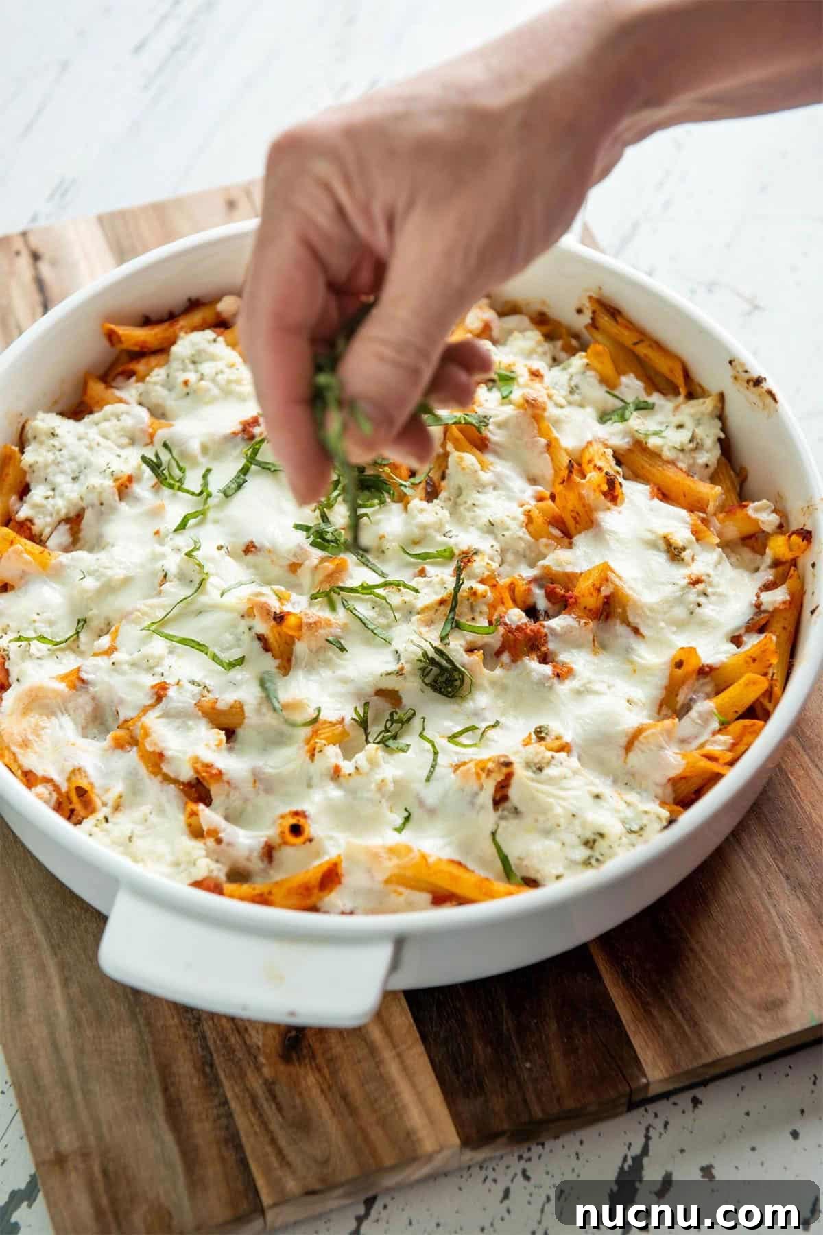 Ultimate Baked Pasta Recipes for Crowd-Pleasing Dinners 3 Woman sprinkling thinly-sliced basil onto a dish of Baked Pasta with Bolognese Sauce.