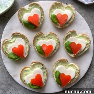 Caprese Bites: Fresh Tomato, Mozzarella & Basil Skewers 4 Seven heart-shaped Caprese Bites are arranged on a round white platter.