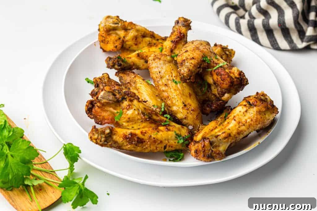 Crispy Air Fryer Chicken Wings — Extra Crunch in 25 Minutes 11 Air fryer chicken wings served on a white plate garnished with parsley.