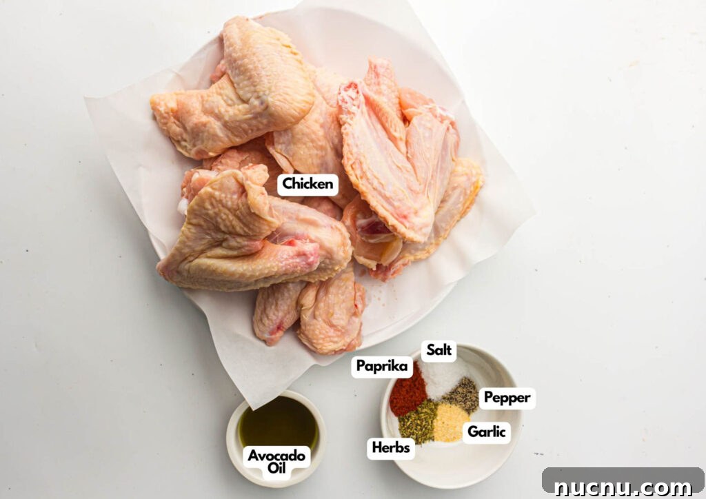 Crispy Air Fryer Chicken Wings — Extra Crunch in 25 Minutes 3 Raw chicken wings on a plate with small bowls of avocado oil, paprika, herbs, salt, pepper, and garlic set beside them—perfect for making flavorful air fryer chicken wings on a white surface.