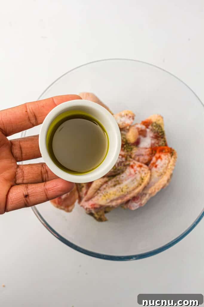 Crispy Air Fryer Chicken Wings — Extra Crunch in 25 Minutes 5 Chicken wings in a bowl with seasonings and a cup of avocado oil.