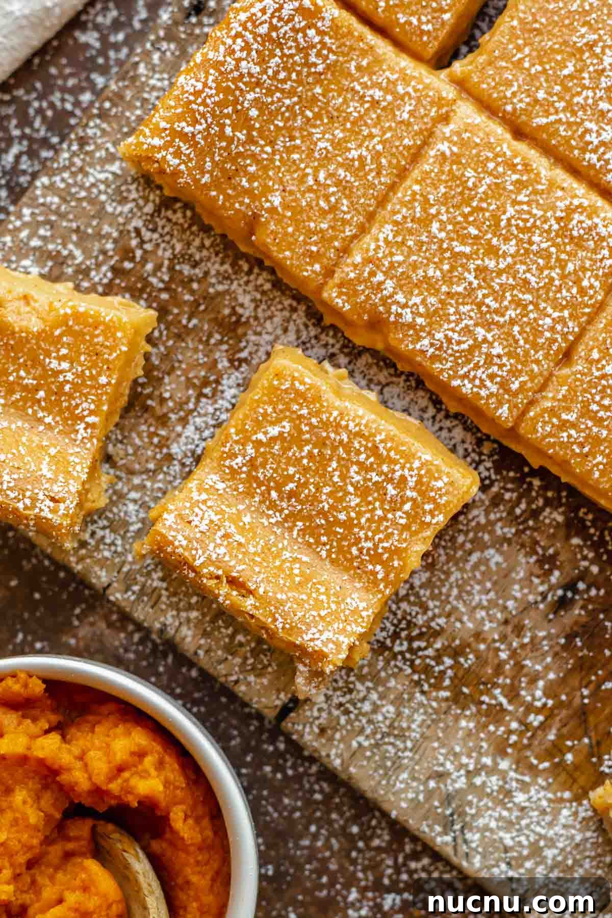 Pumpkin gooey bars on a cutting board, sliced. Powdered sugar is dusted on top.