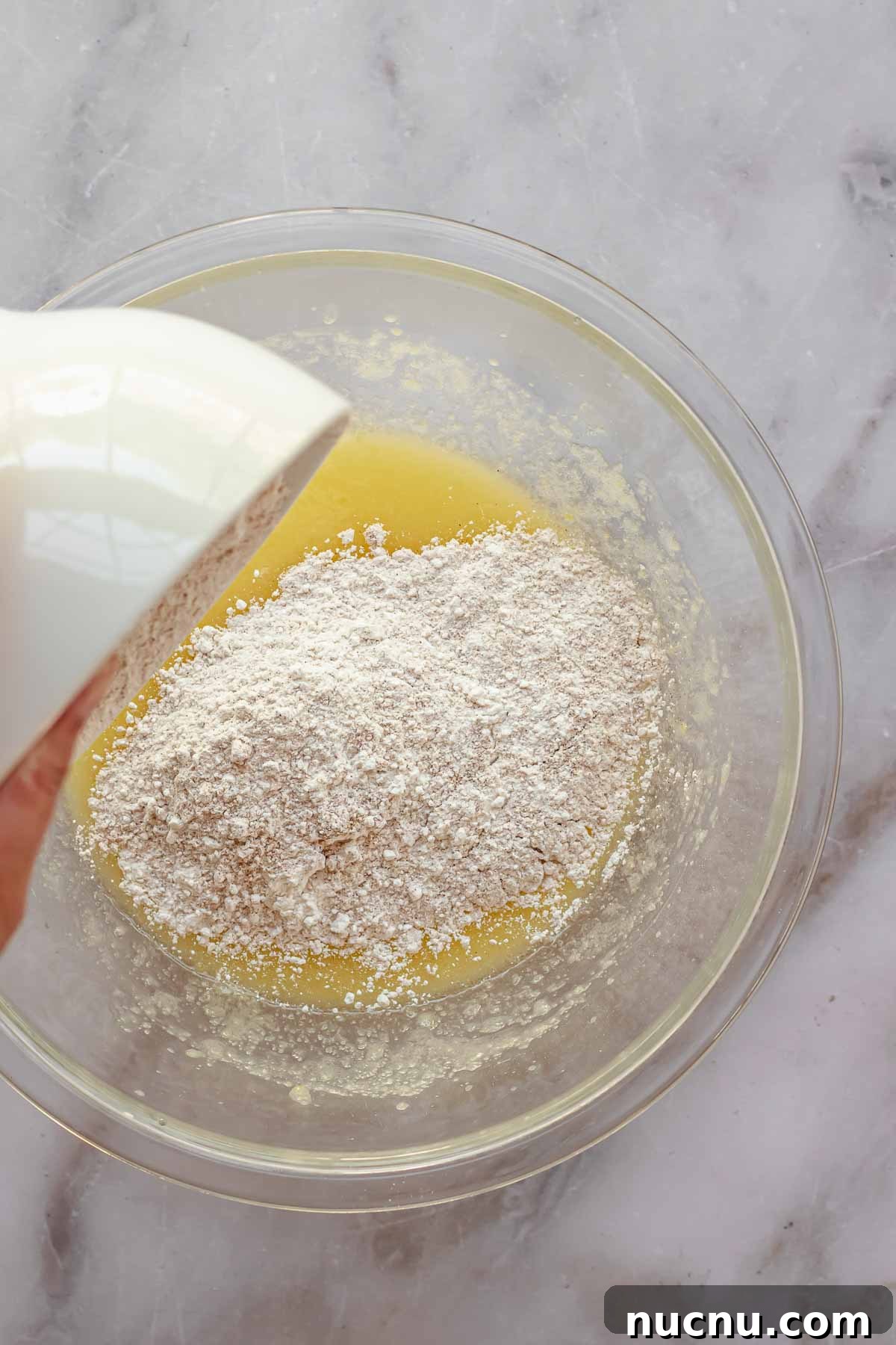 A bowl of flour being poured into a bowl of wet ingredients.