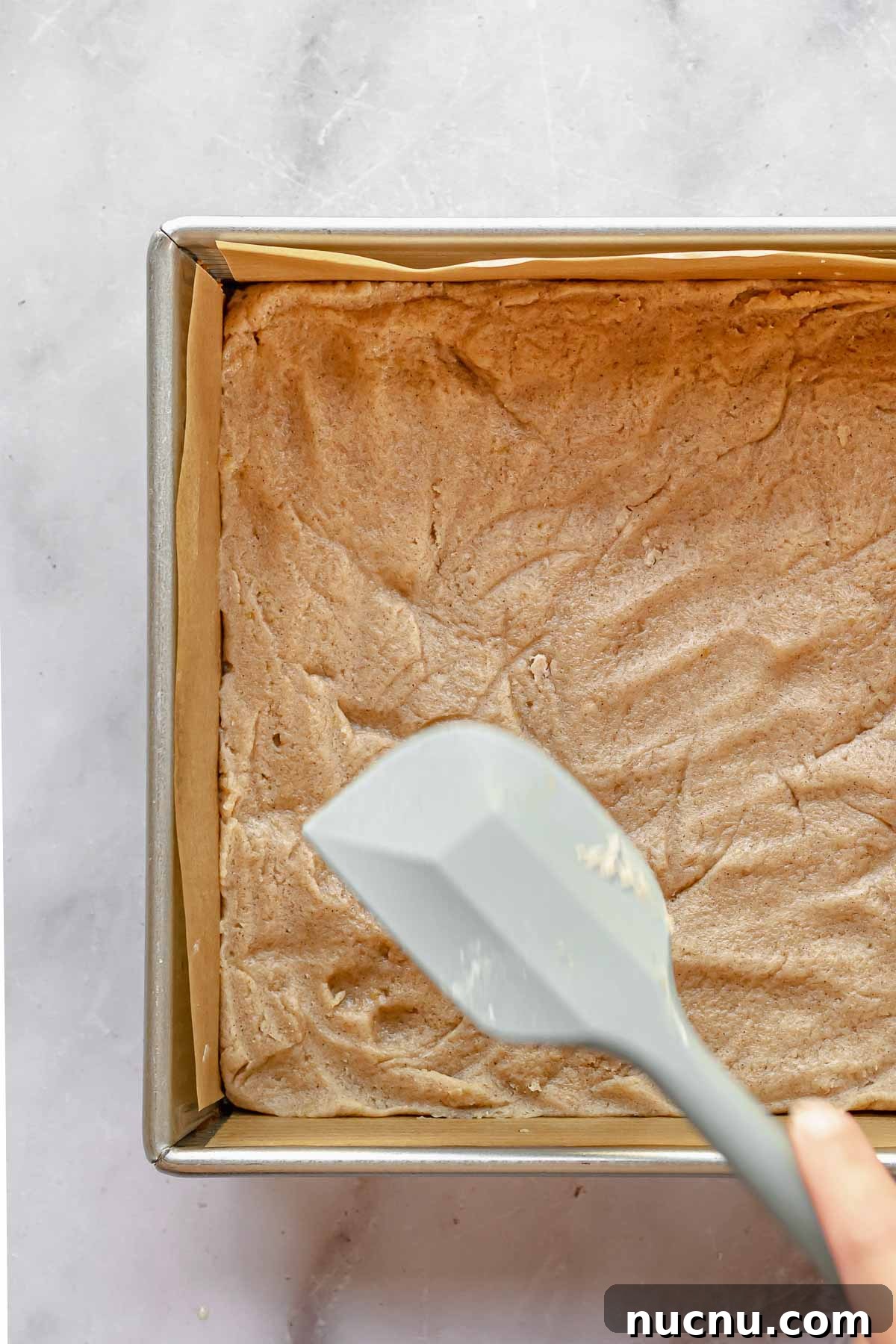 A spatula pushes dough in to a square baking pan.