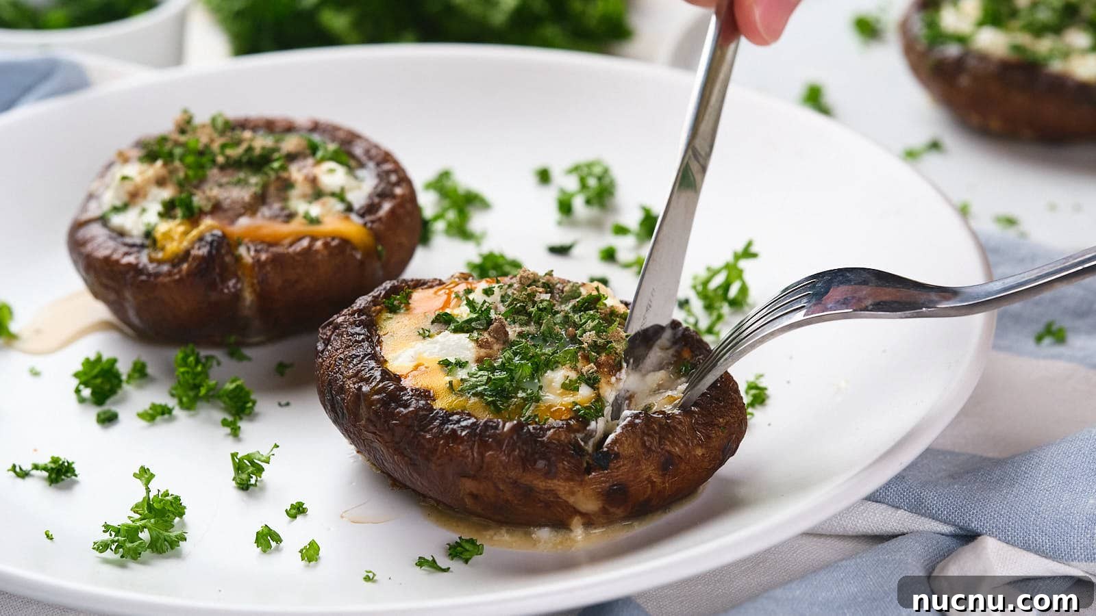 A fork and knife cutting into an egg in mushroom with green garnish visible in the background.