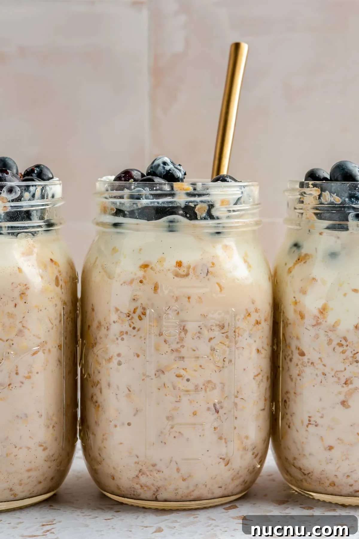 3 mason jars, full of high protein overnight oats, have been topped with blueberries.