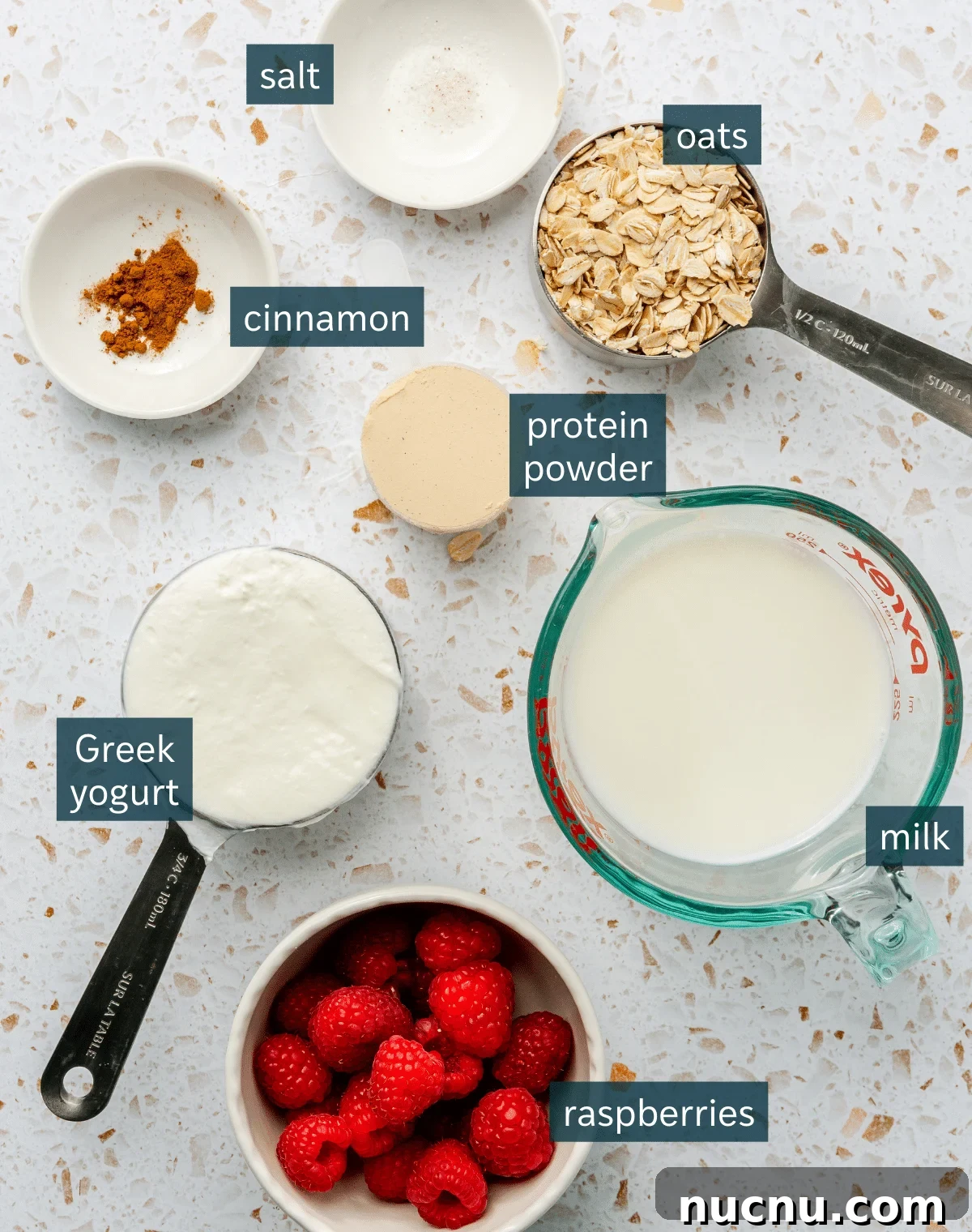 All of the ingredients needed for high protein oatmeal in different sized bowls and plates on a terrazzo surface.