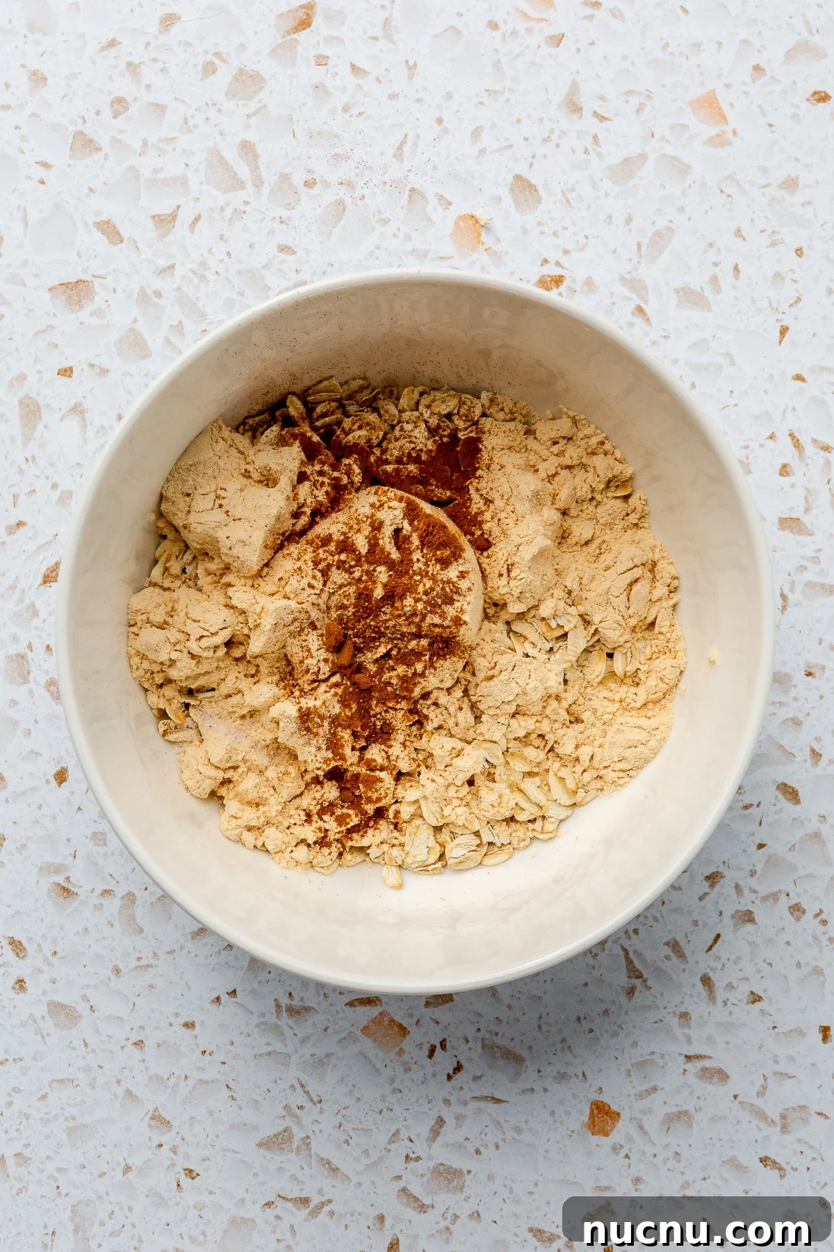 Ingredients for hot protein oatmeal have been placed into a white mixing bowl.