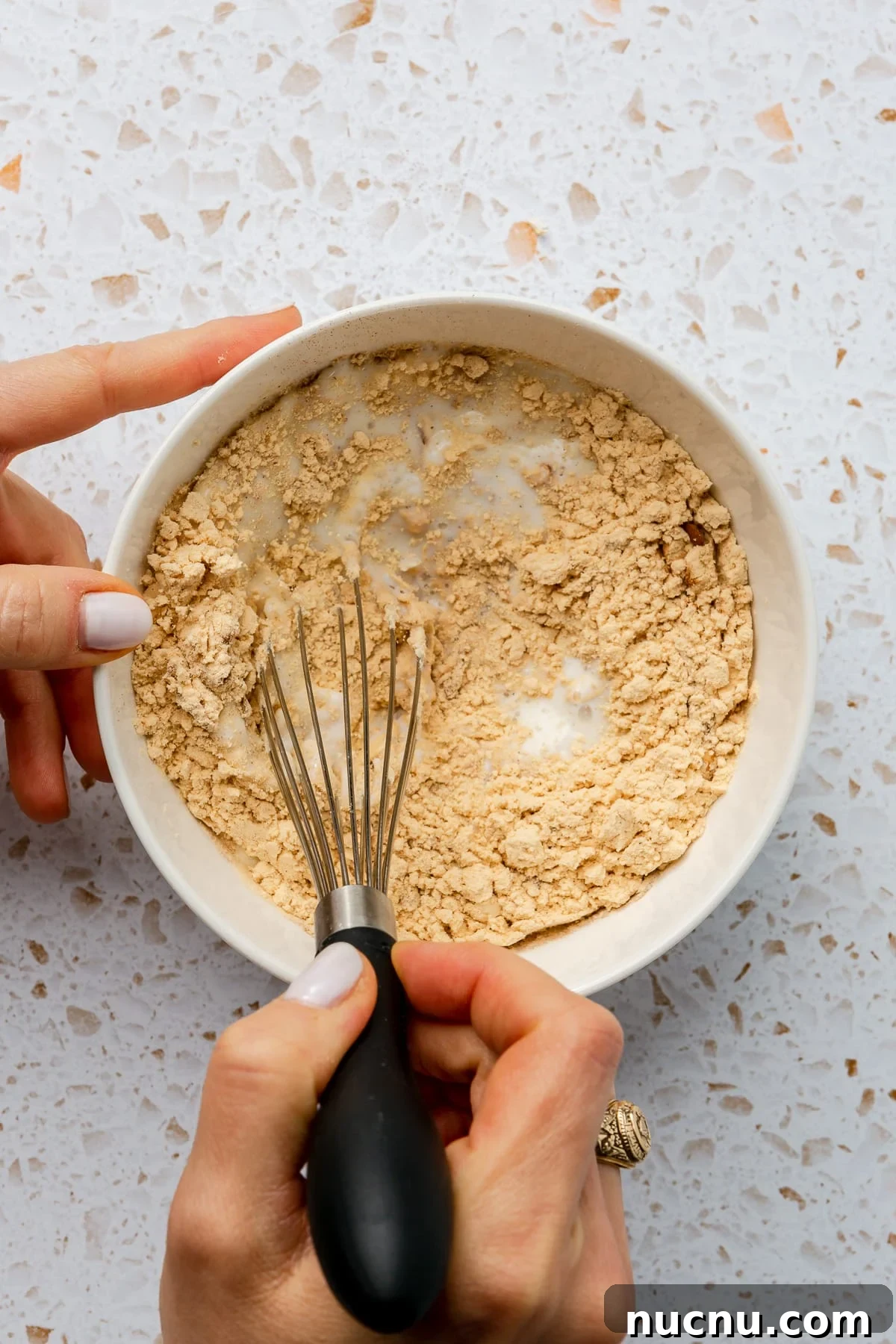 Two hands are shown whisking the ingredients together.